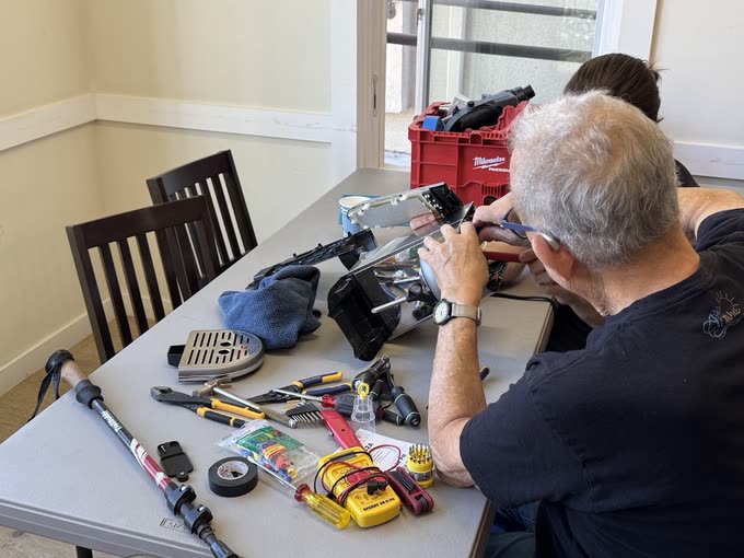 A volunteer with gray hair carefully repairing a coffee machine at a table covered with tools